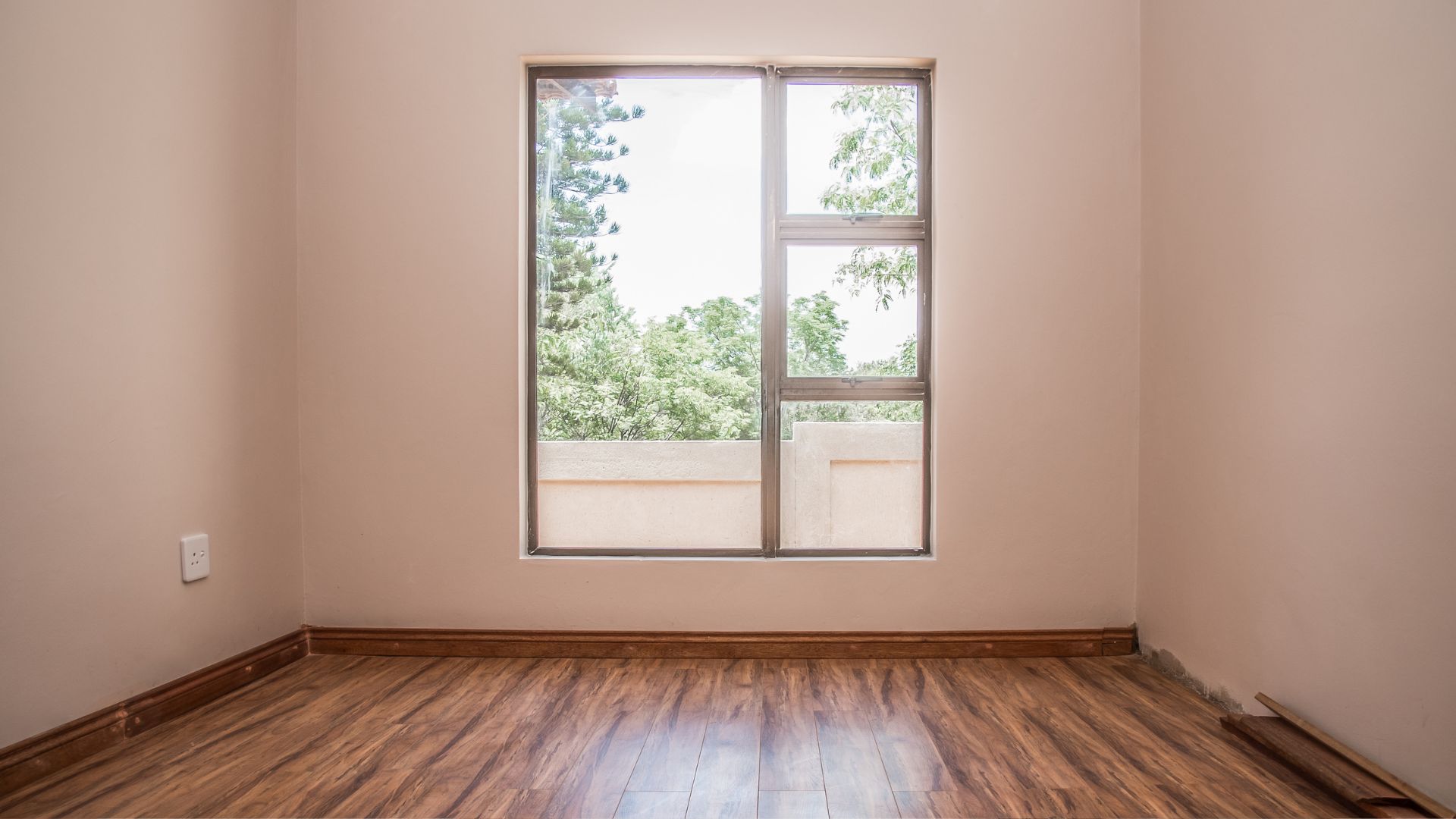 A empty room with a window and hard wood floor