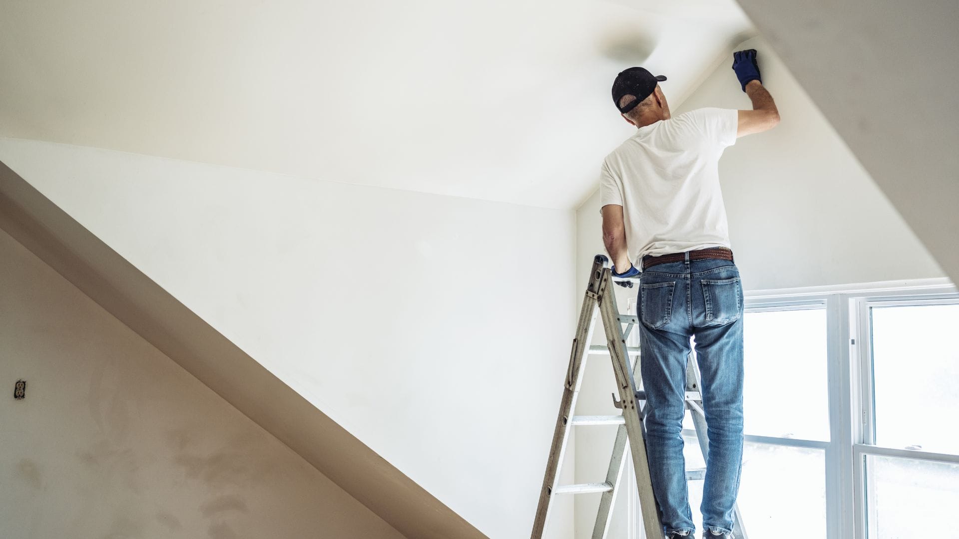 Painter on a ladder finishing a smooth white ceiling