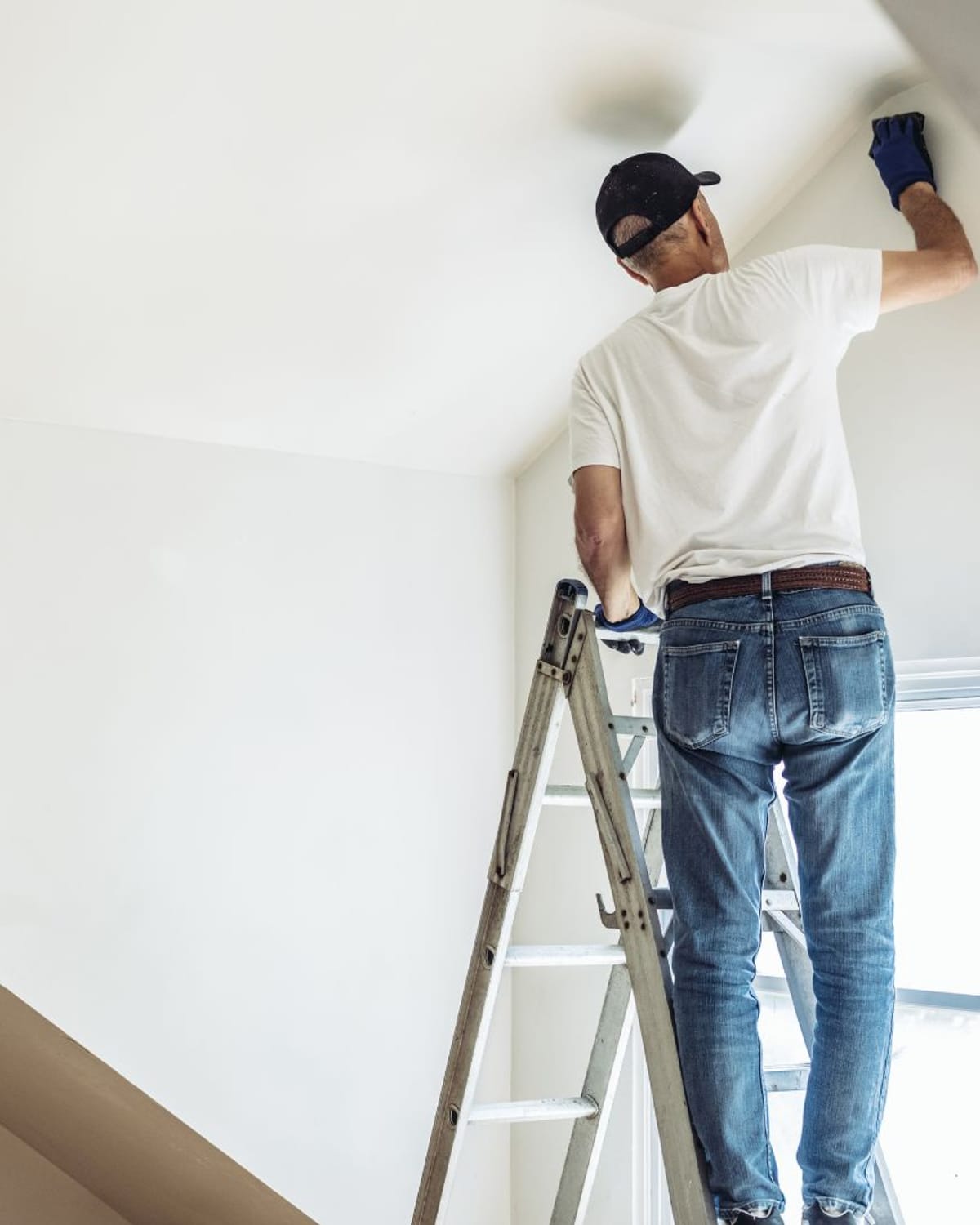 Painter on a ladder finishing a freshly textured and painted sloped ceiling