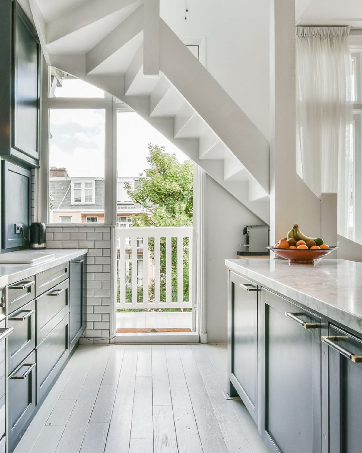 Kitchen with dark painted lower cabinets, white subway tile and marble counters